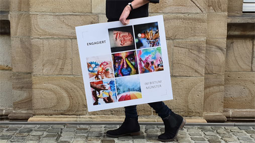 Bild einer Person, die ein Plakat trägt. Auf dem Plakat sind verschiedene kleinere Fotos als Collage zu sehen und die Überschrift "Engagiert im Bistum Münster"