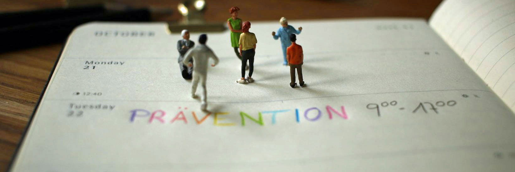 Kalender mit einem Eintrag "Prävention" aus bunten Buchstaben - auf dem Kalender sieht man Miniaturfiguren, die miteinander zu sprechen scheinen.